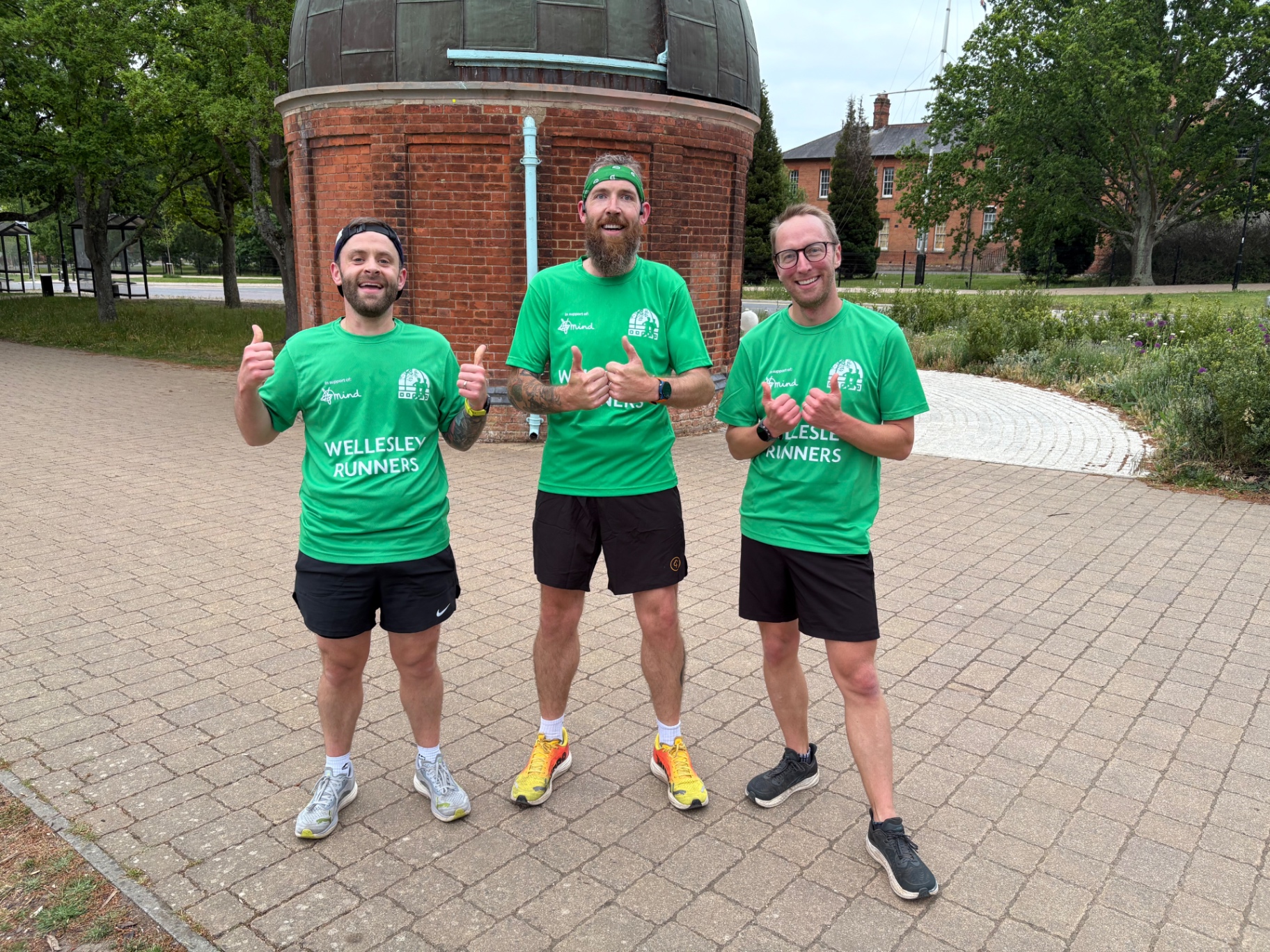 Three Wellesley Runners in club tees giving a thumbs up before a social run