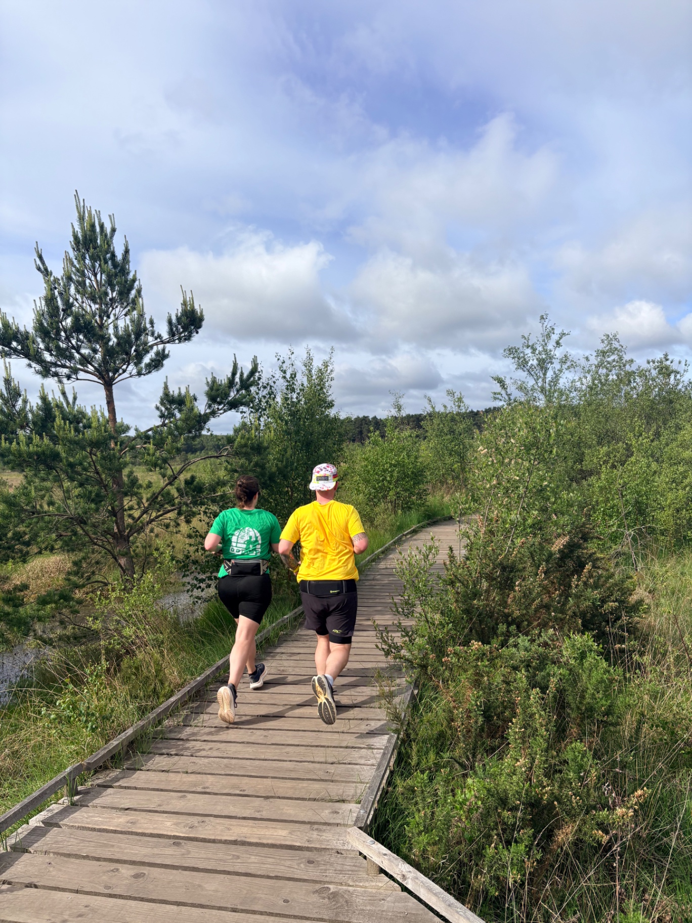 Two Wellesley Runners jogging side by side along a wooden boardwalk trail